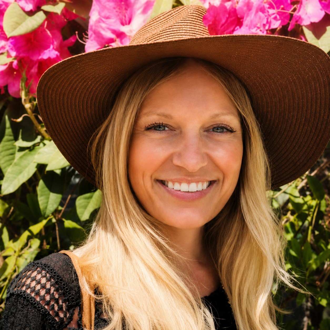 Kaitlyn Krahn smiling in a sun hat in front of bright pink bougainvillea, self portrait.